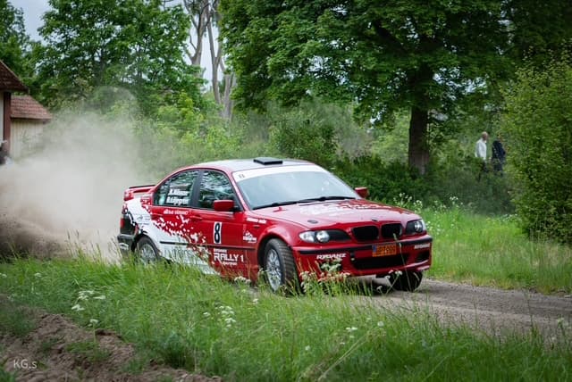 Rallybil sladdar förbi en röd lada i ett moln av grus